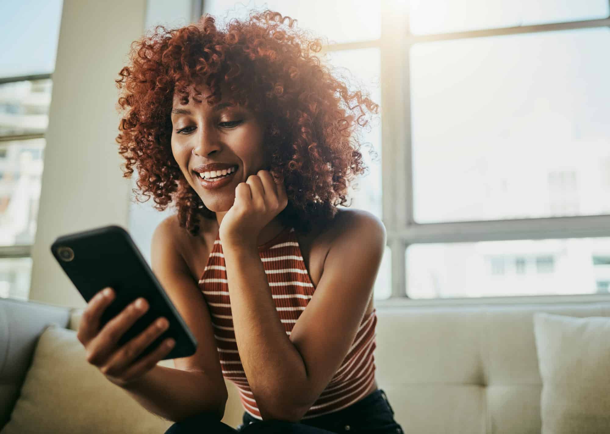 A woman scrolls on her phone on the couch.