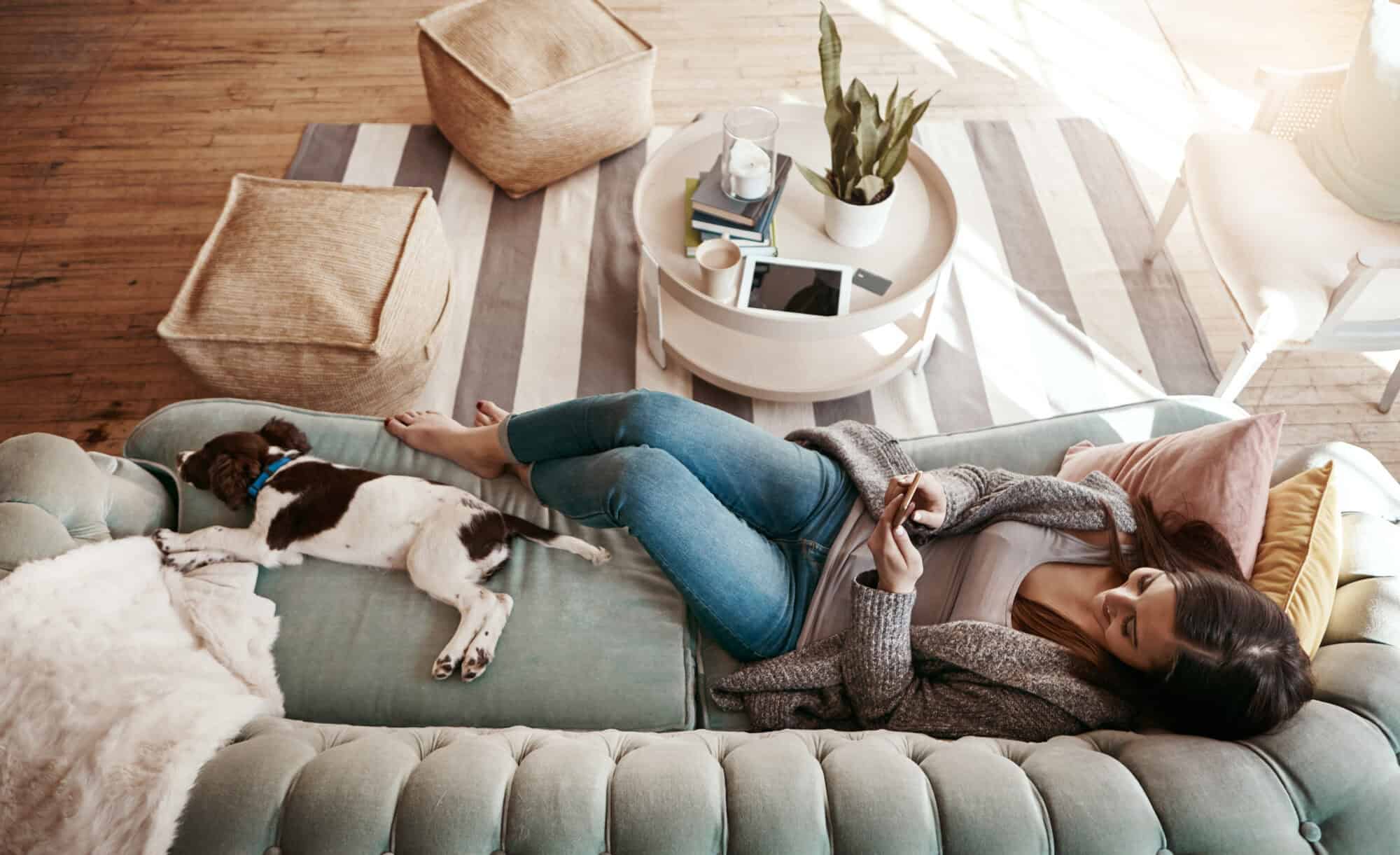 A woman searching on her phont with her dog nearby.